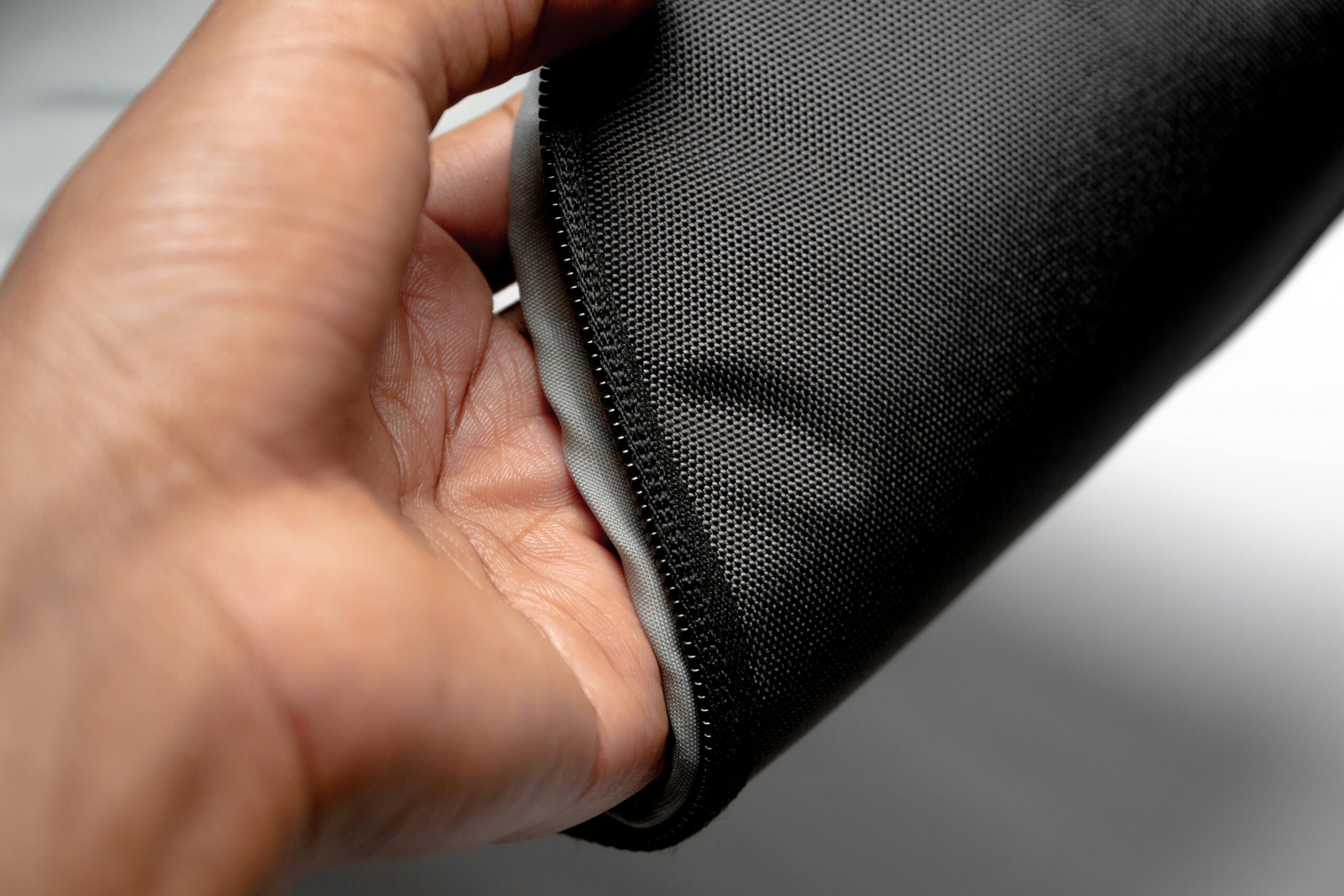 Detailed close-up of a hand holding a waterproof black textile material with zipper.