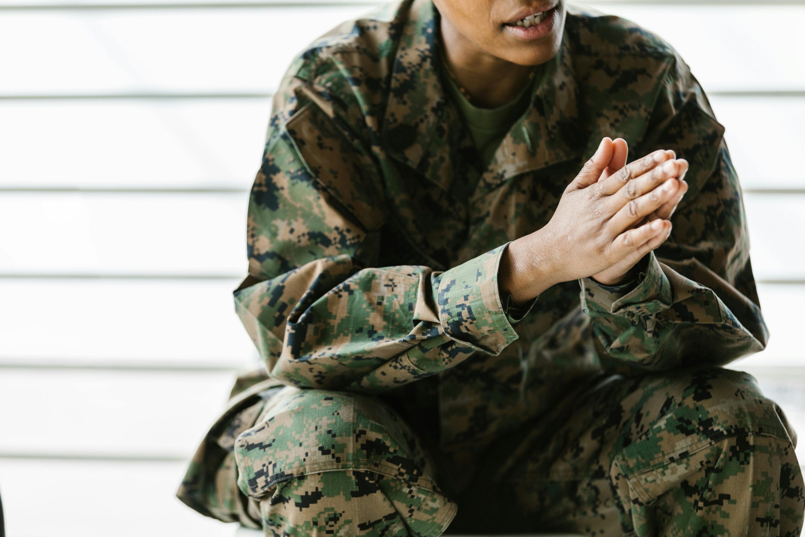 A close-up view of a soldier sitting in a camouflage uniform with clasped hands.