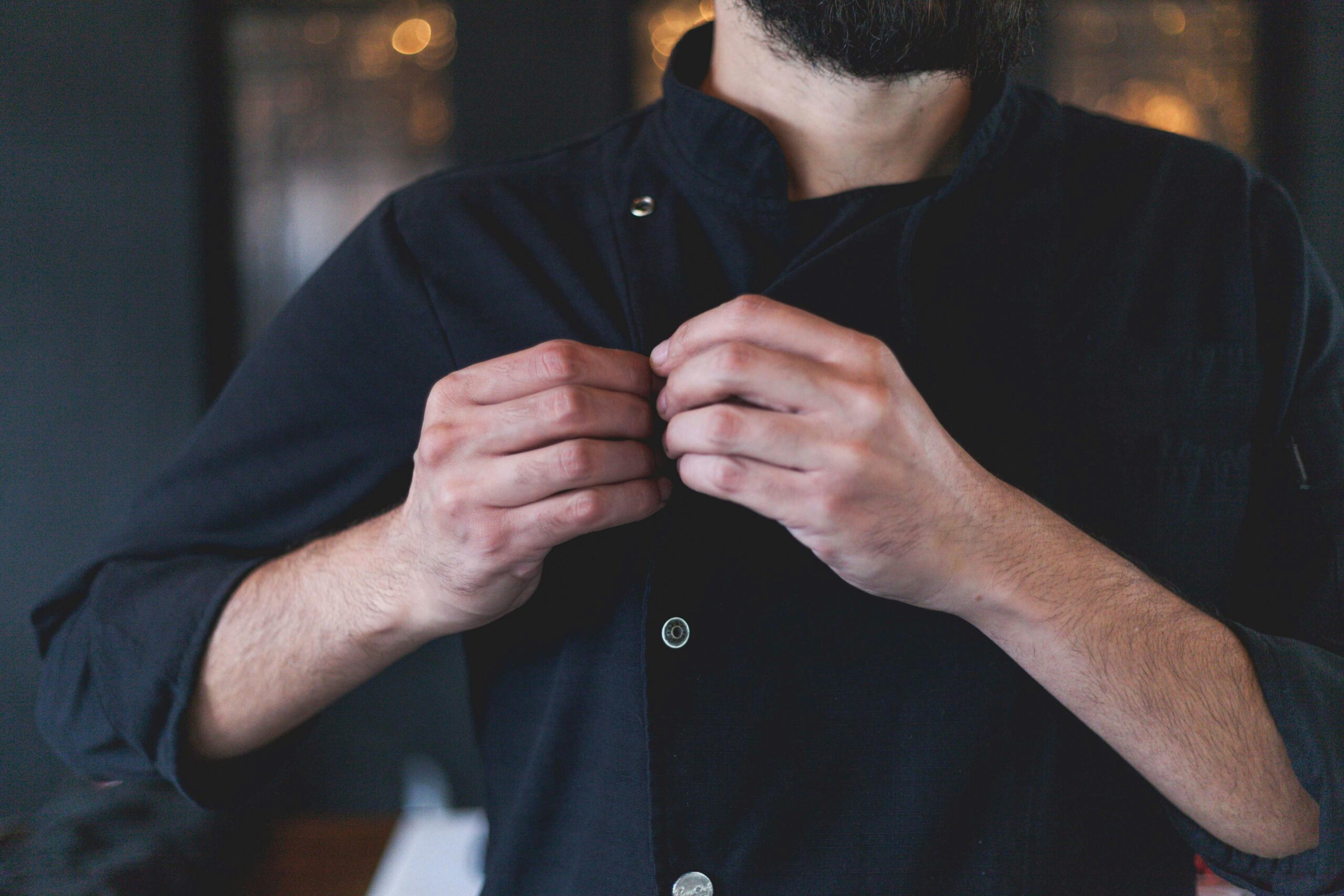 Close-up of a chef fastening buttons on a dark uniform in a cozy kitchen.